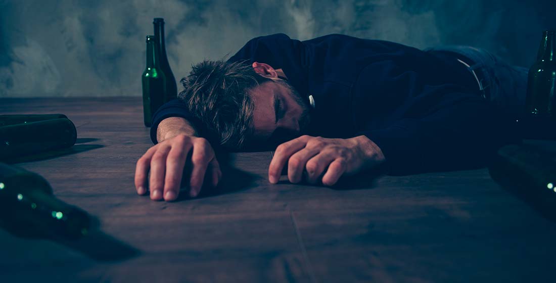 пьяный мужчина спит на полу в окружении бутылок